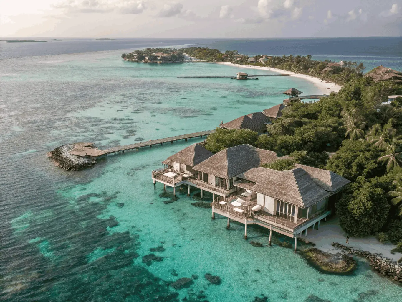 A stunning aerial view of a luxury resort in the Maldives, showcasing crystal-clear turquoise waters, pristine white sandy beaches, and overwater bungalows. The image should convey a sense of exclusivity, relaxation, and tropical paradise.
